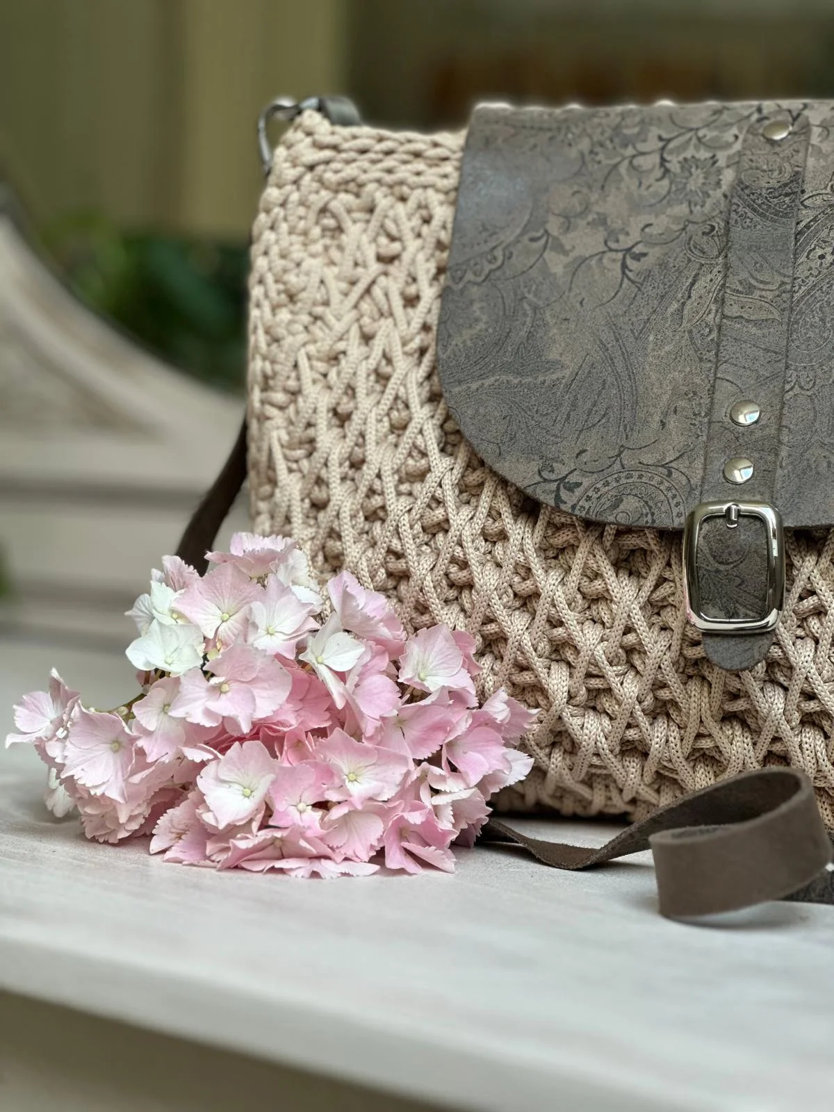 Beiger Häkelrucksack mit grau geprägtem Lederdeckel und silberner Schnalle, mit rosa Hortensie